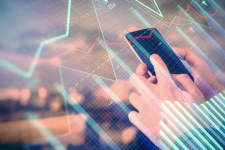Double exposure of mans hands holding and using a digital device and forex graph drawing. Financial...