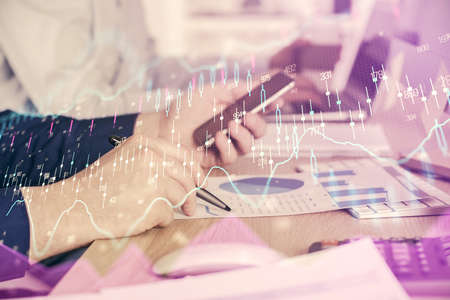 Double exposure of mans hands holding and using a digital device and forex graph drawing. Financial...