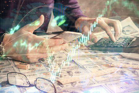 Double exposure of mans hands holding and using a digital device and forex graph drawing. Financial market concept.の写真素材