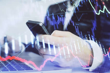 Multi exposure of mans hands holding and using a digital phone and forex graph drawing. Financial...
