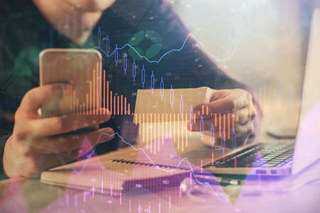 Double exposure of mans hands holding and using a phone and financial graph drawing. Analysis...