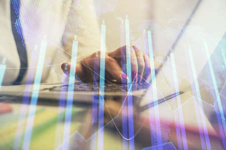 Double exposure of businesswoman hands typing on computer and financial graph hologram drawing....