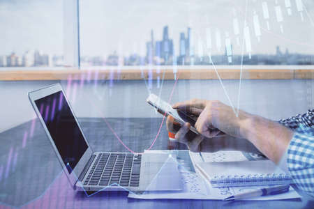 Double exposure of mans hands holding and using a digital device and forex graph drawing. Financial...