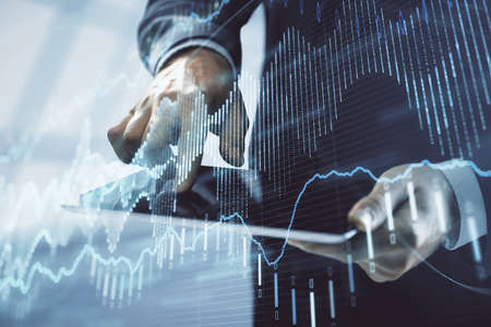 Double exposure of mans hands holding and using a digital device and forex graph drawing. Financial...