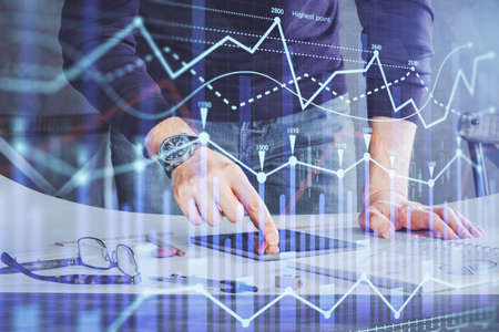 Double exposure of mans hands holding and using a digital device and forex graph drawing. Financial...