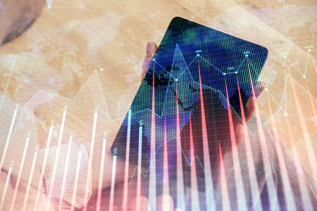 Double exposure of mans hands holding and using a digital device and forex graph drawing. Financial...