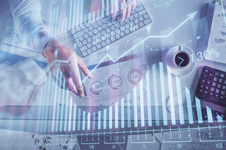 Multi exposure of mans hands typing over computer keyboard and forex graph hologram drawing. Top...