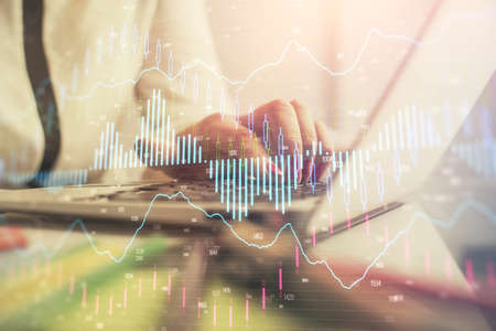 Double exposure of businesswoman hands typing on computer and financial graph hologram drawing....