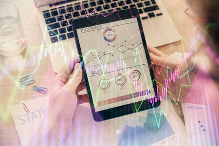 Double exposure of mans hands holding and using a digital device and forex graph drawing. Financial...