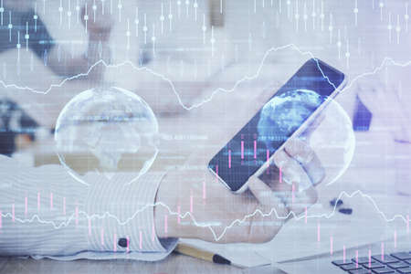Double exposure of mans hands holding and using a digital device and forex graph drawing. Financial...