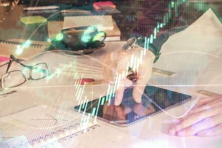 Double exposure of mans hands holding and using a digital device and forex graph drawing. Financial...