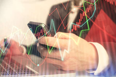Multi exposure of mans hands holding and using a digital phone and forex graph drawing. Financial...