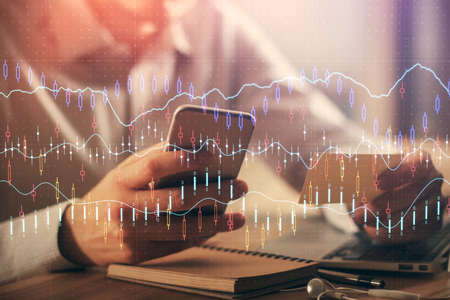 Double exposure of mans hands holding and using a phone and financial graph drawing. Analysis...