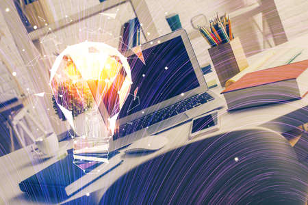 Computer on desktop in office with bulb icon hologram. Double exposure. Concept of idea.