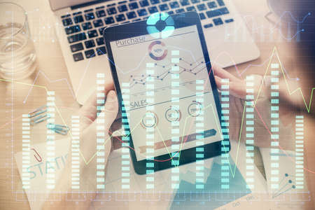 Double exposure of mans hands holding and using a digital device and forex graph drawing. Financial...