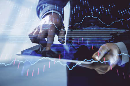 Double exposure of mans hands holding and using a digital device and forex graph drawing. Financial...