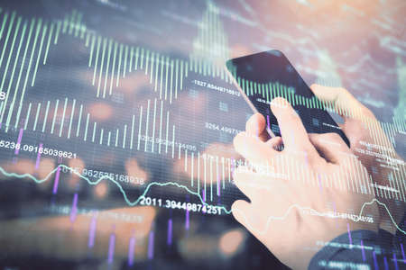 Double exposure of mans hands holding and using a digital device and forex graph drawing. Financial...