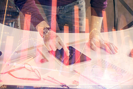 Double exposure of mans hands holding and using a digital device and forex graph drawing. Financial...
