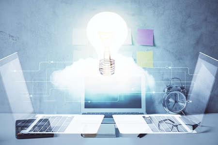 Computer on desktop in office with bulb icon hologram. Double exposure. Concept of idea.
