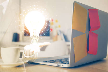 Computer on desktop in office with bulb icon hologram. Double exposure. Concept of idea.の写真素材