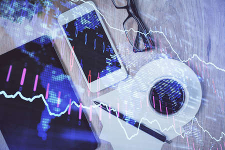 Double exposure of forex chart hologram over desktop with phone. Top view. Mobile trade platform...
