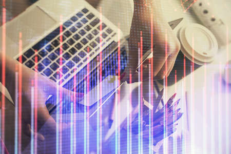 Double exposure of businesswoman hands typing on computer and financial graph hologram drawing....
