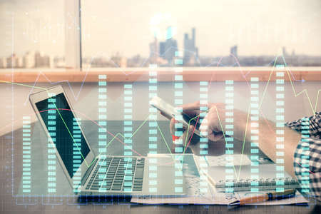 Double exposure of mans hands holding and using a digital device and forex graph drawing. Financial...
