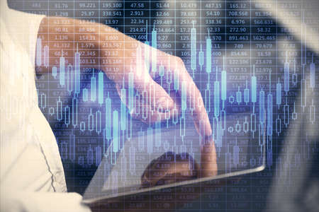 Double exposure of mans hands holding and using a digital device and forex graph drawing. Financial...