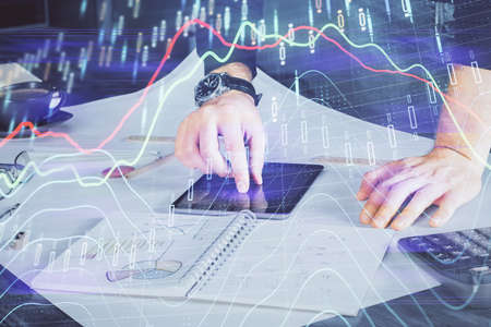 Double exposure of mans hands holding and using a digital device and forex graph drawing. Financial...