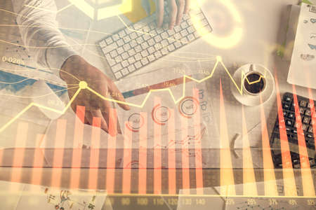 Multi exposure of mans hands typing over computer keyboard and forex graph hologram drawing. Top...