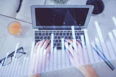 Double exposure of mans hands typing over laptop keyboard and forex chart hologram drawing. Top...