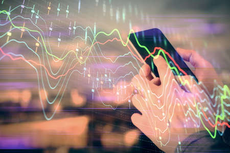 Double exposure of mans hands holding and using a digital device and forex graph drawing. Financial...