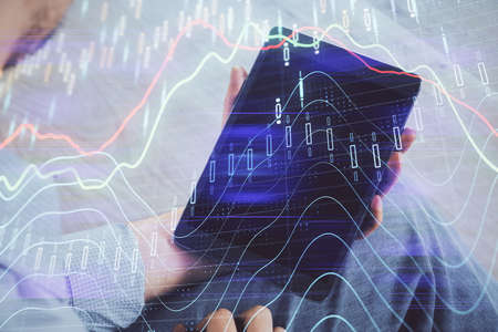 Double exposure of mans hands holding and using a digital device and forex graph drawing. Financial...