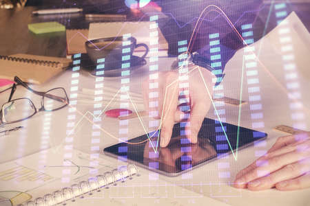Double exposure of mans hands holding and using a digital device and forex graph drawing. Financial...