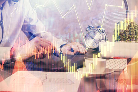 Double exposure of mans hands holding and using a phone and financial graph drawing. Analysis...