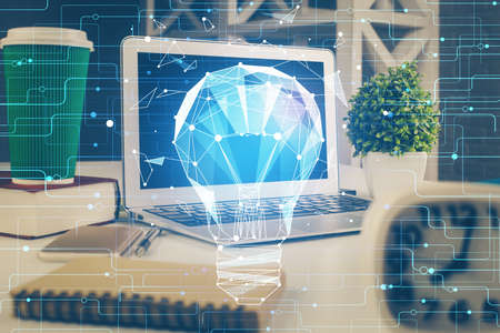 Computer on desktop in office with bulb icon hologram. Double exposure. Concept of idea.