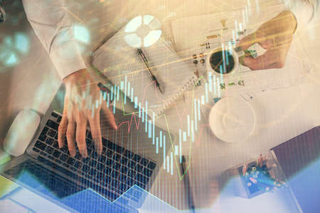 Multi exposure of mans hands typing over computer keyboard and forex graph hologram drawing. Top...