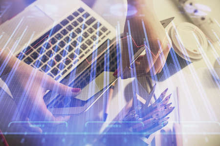 Double exposure of businesswoman hands typing on computer and financial graph hologram drawing....
