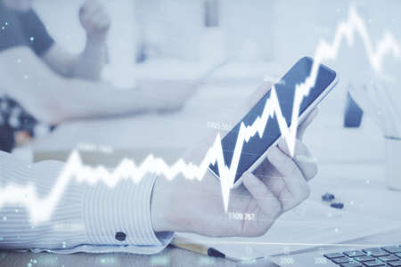 Double exposure of mans hands holding and using a digital device and forex graph drawing. Financial...