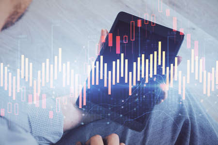 Double exposure of mans hands holding and using a digital device and forex graph drawing. Financial...