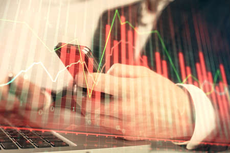 Multi exposure of mans hands holding and using a digital phone and forex graph drawing. Financial...