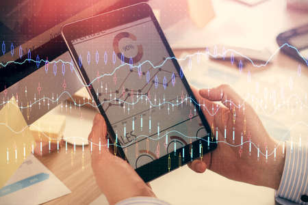 Double exposure of mans hands holding and using a phone and financial graph drawing. Analysis...
