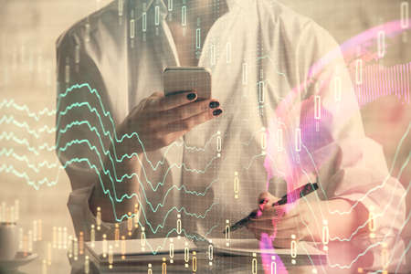 Double exposure of financial graph sketch hologram and woman holding and using a mobile device....