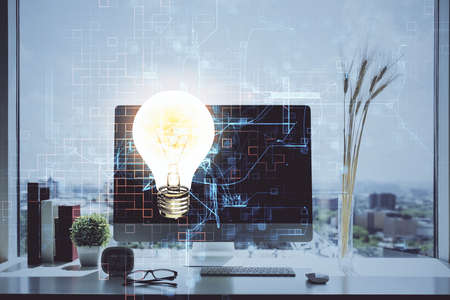 Computer on desktop in office with bulb icon hologram. Double exposure. Concept of idea.の写真素材