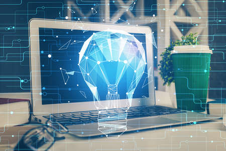 Computer on desktop in office with bulb icon hologram. Double exposure. Concept of idea.