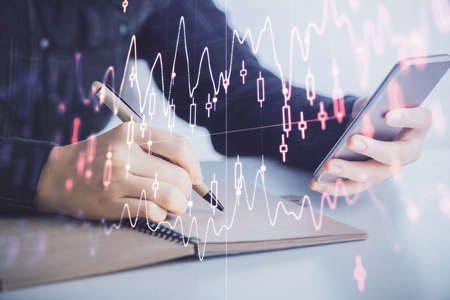 Double exposure of forex graph sketch hologram and woman holding and using a mobile device. Stock...