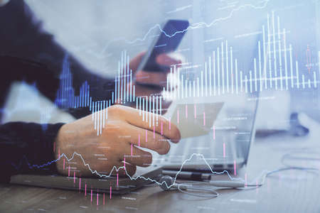 Double exposure of mans hands holding and using a phone and financial graph drawing. Analysis...