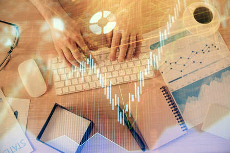 Multi exposure of mans hands typing over computer keyboard and forex graph hologram drawing. Top...
