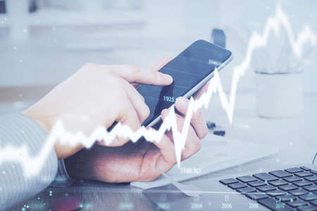 Double exposure of mans hands holding and using a digital device and forex graph drawing. Financial...