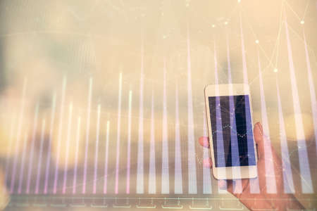 Double exposure of forex chart sketch hologram and woman holding and using a mobile device. Stock market concept.の写真素材
